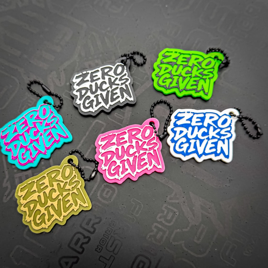 Six vibrant Zero Ducks Given Keychains by FirstWarrior, crafted from PLA plastic and shaped like speech bubbles, are displayed on a dark surface. Fun 3D printed gifts or quirky accessories for your car dashboard.