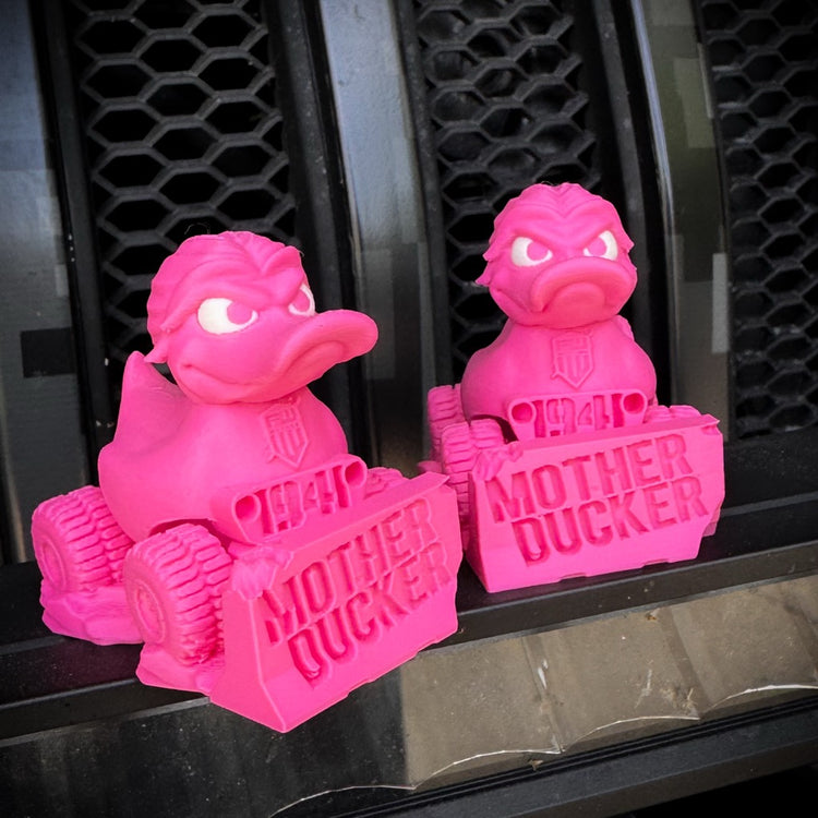 Two vibrant pink Mother Ducker - v2.0 figurines by FirstWarrior, 3D-printed in PLA with fierce looks, sit on labeled toy car bases in front of a black vented surface—perfect for any limited edition collection.