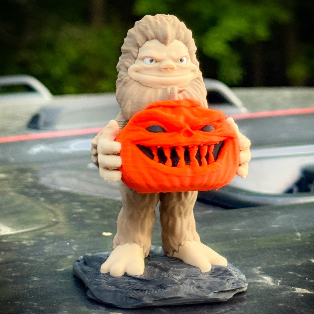 The FirstWarrior Pumpkin Patch Bigfoot figurine stands on a black base, holding an orange jack-o’-lantern—an eye-catching Halloween accessory for your Jeep.