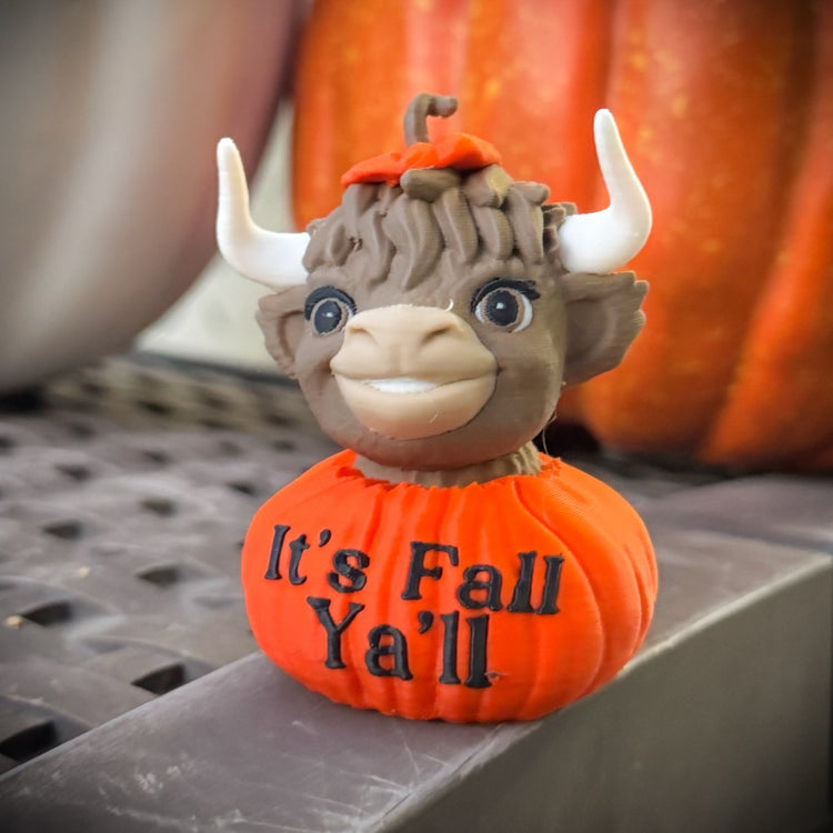 Pumpkin with a cartoonish animal face and 'It's Fall Ya'll' text, with a blurred pumpkin in the background.
