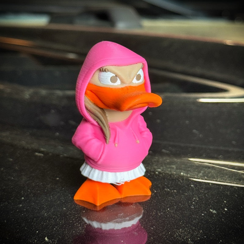 Toy figure of a duck character wearing a pink hoodie on a reflective surface.