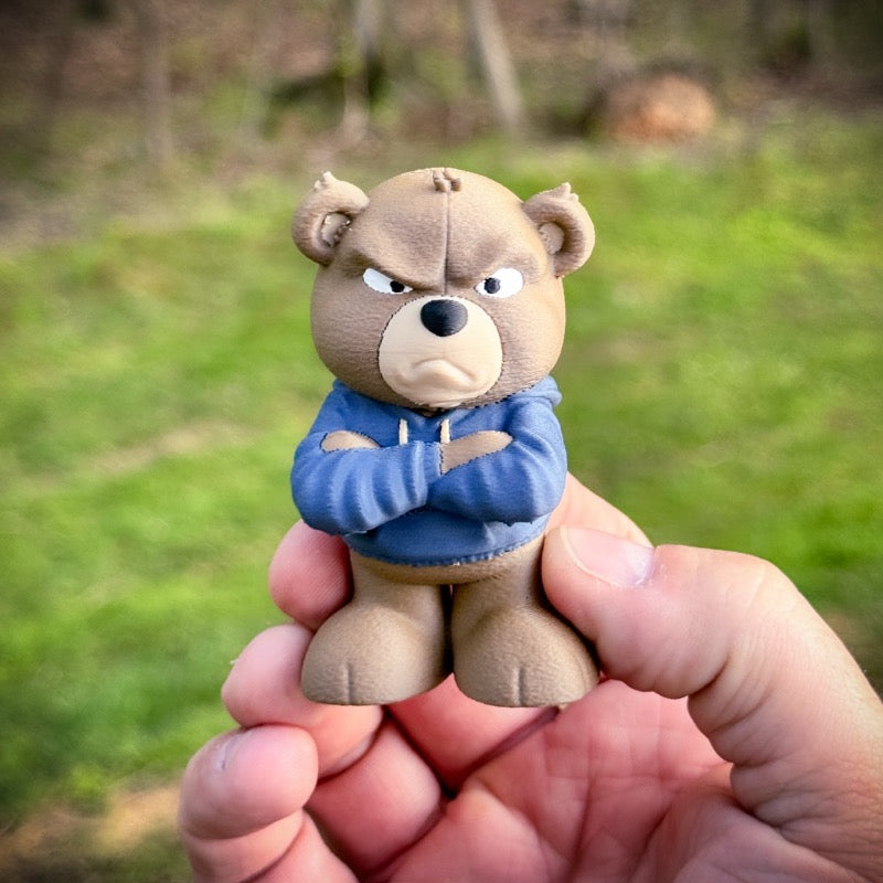 Small bear figurine wearing a blue sweater held in a hand with a blurred natural background