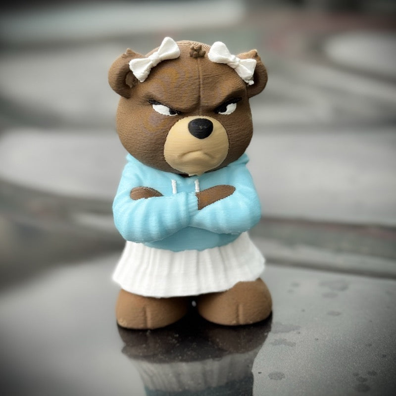 Teddy bear wearing a blue hoodie and white skirt with a bow on a reflective surface.