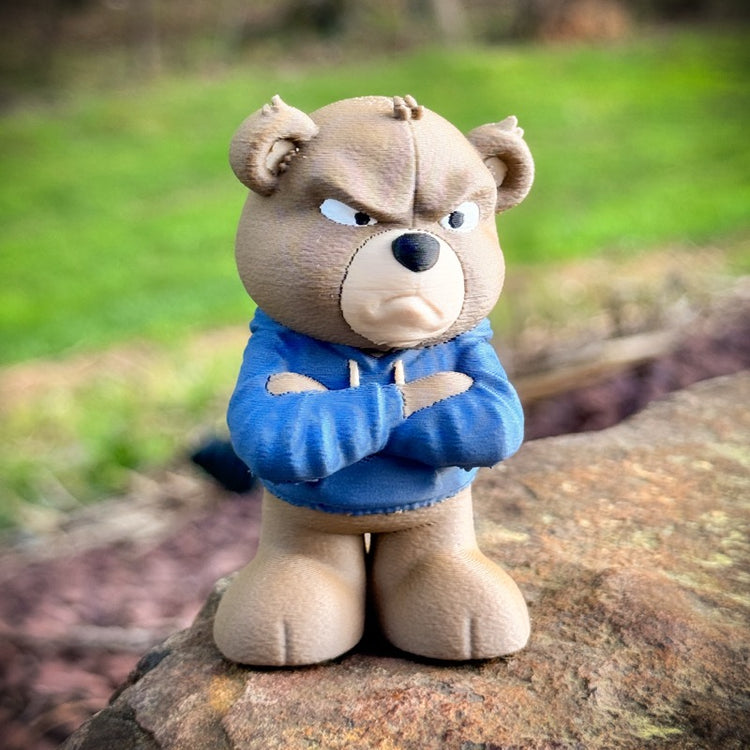 Plush bear toy wearing a blue sweater standing on a rock with a natural background
