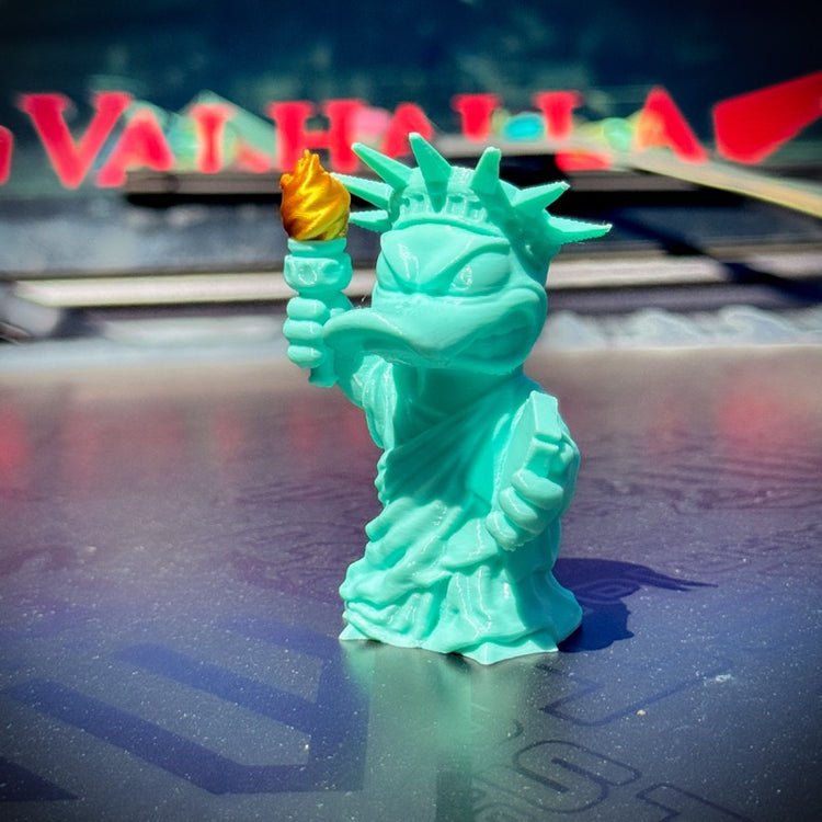 Turquoise statue of a duck holding a torch on a reflective surface with blurred background