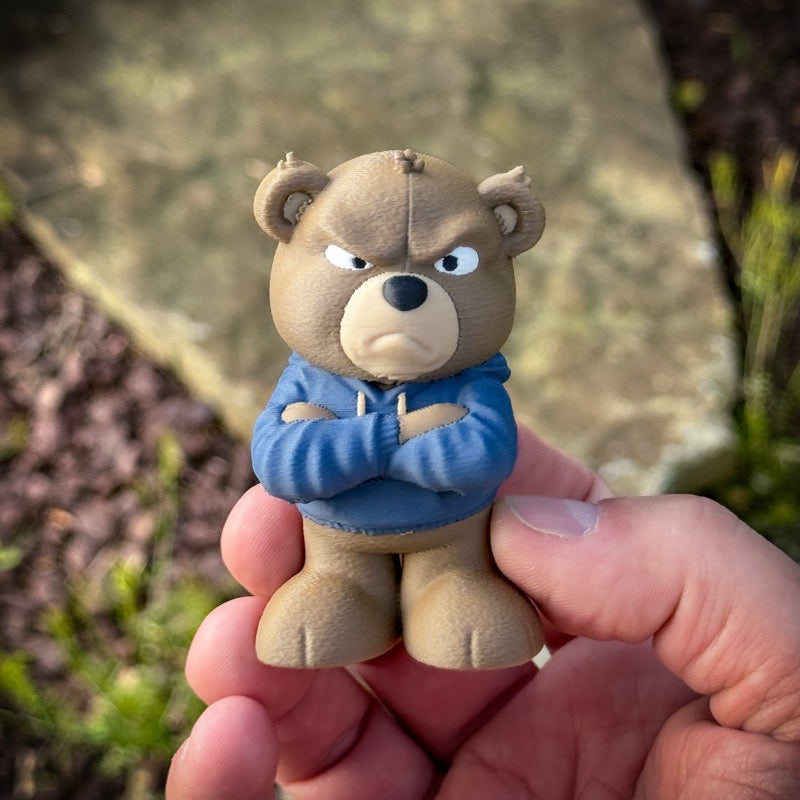 Small bear figurine wearing a blue sweater held in a hand with a natural background