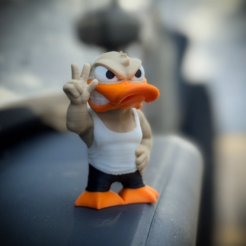 The FirstWarrior Tough Guy Duck is a small PLA figurine for your car dashboard, wearing a white tank top and black pants, confidently holding up three fingers with a determined look. Features blurred background for stylish display.