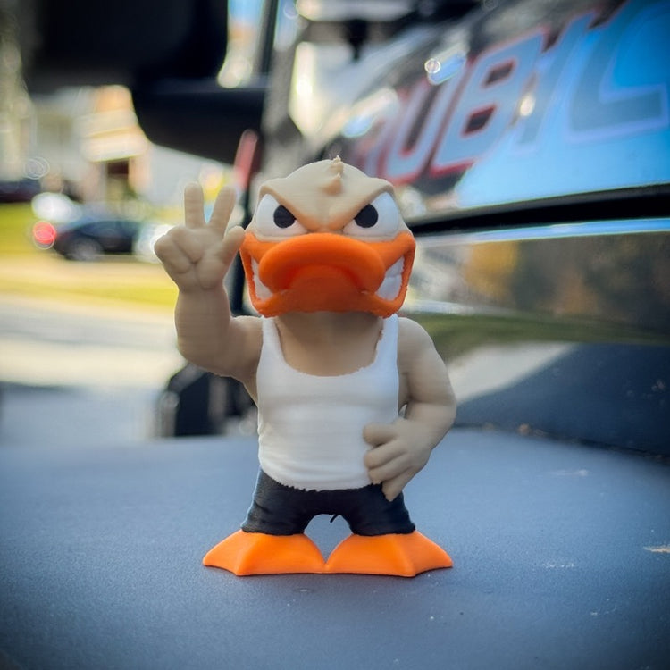 The FirstWarrior Tough Guy Duck, a small PLA dashboard accessory, stands outdoors in a white tank top and black shorts, one hand on its hip and the other showing a peace sign by a shiny, dark surface.