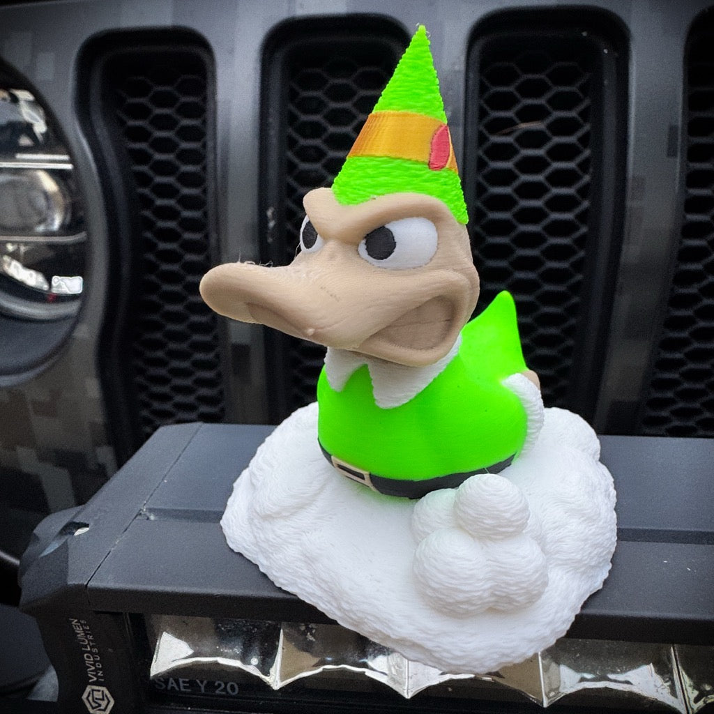 Buddy the Duck by FirstWarrior features an angry expression and a green elf costume with a pointy hat, seated on a white, cloud-like base—making it an ideal festive car dashboard accessory or quirky Christmas decoration.