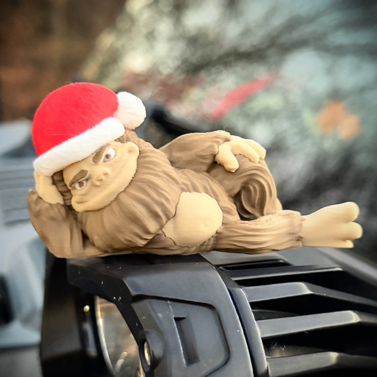 The FirstWarrior Hunky Claus Bigfoot, wearing a red Santa hat, rests atop a black Jeep accessory—a playful holiday gift for off-road fans.