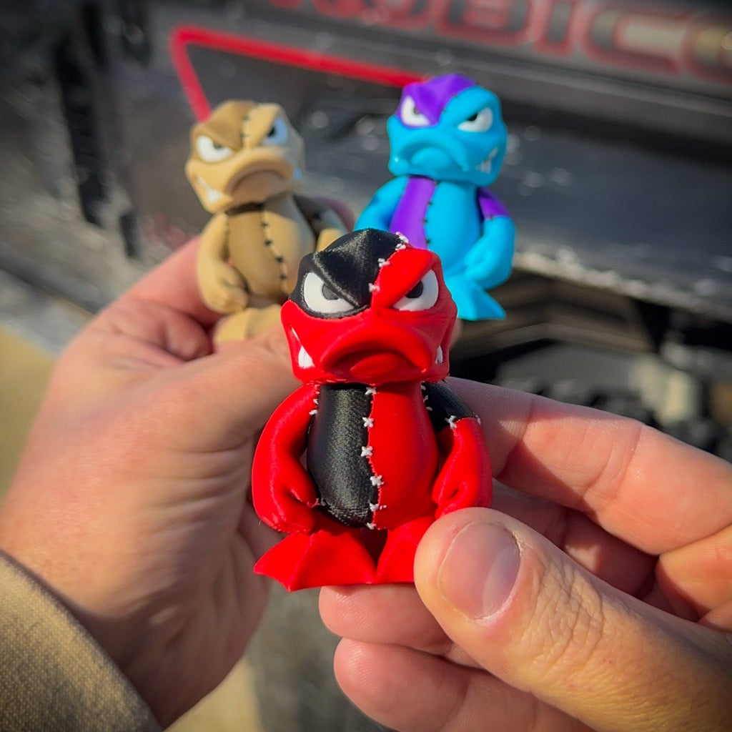 Red toy figure held by a hand with two other toy figures in the background.