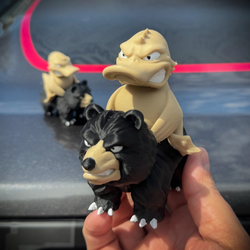 Two toy figures of a black and tan creature held in front of a car.