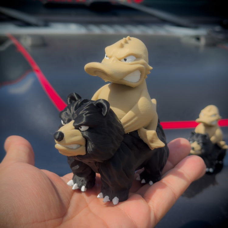 Two toy figures of a bear and a duck on a person's palm with a blurred background.