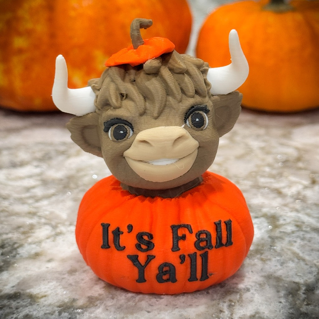 Pumpkin-shaped toy with a bull head and 'It's Fall Ya'll' text, surrounded by pumpkins.